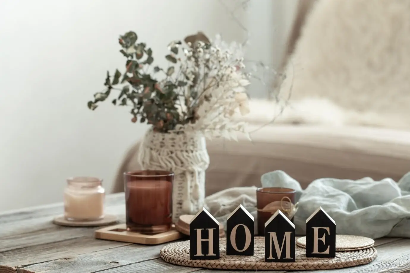 Nahaufnahme des dekorativen Schriftzugs „Home“ vor unscharfem Hintergrund mit Kerzen.